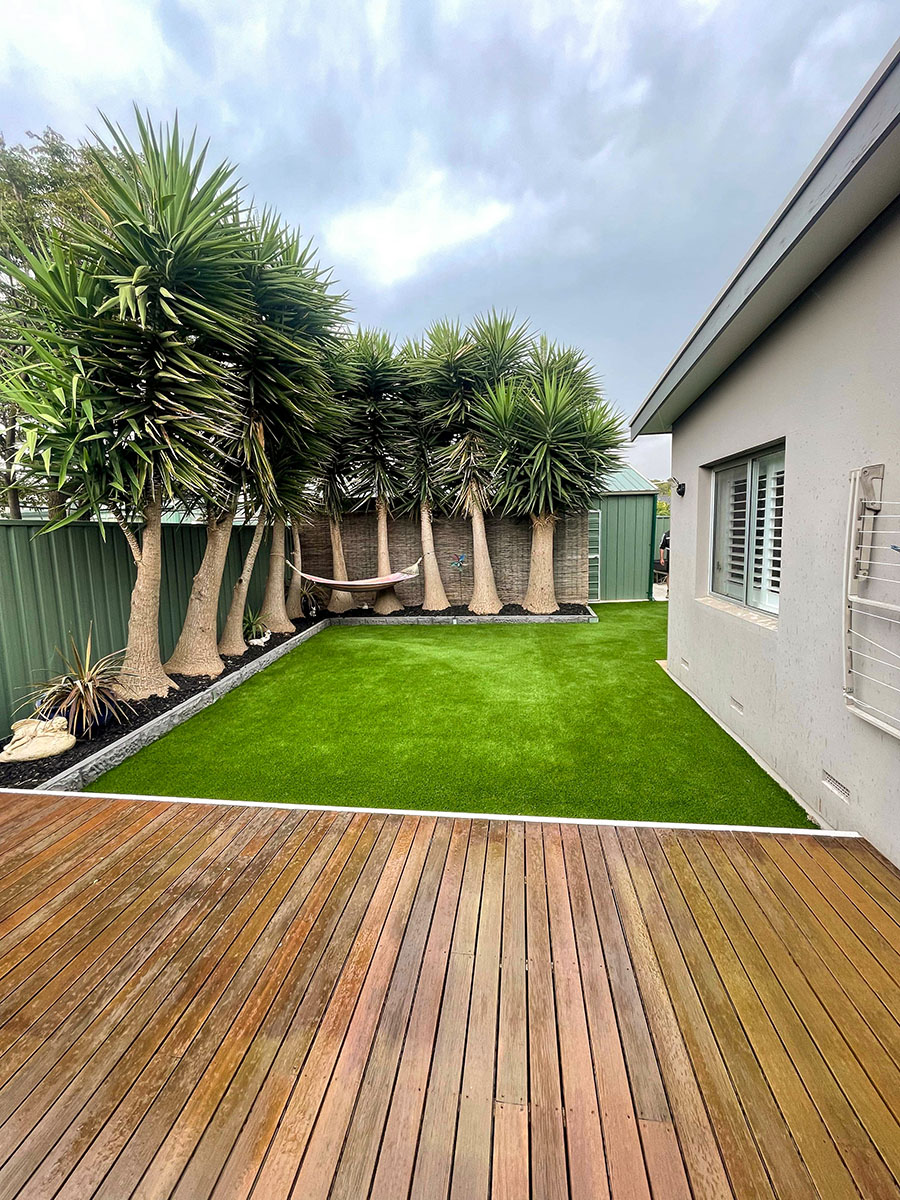 artificial turf next to decking and a garden in a backyard