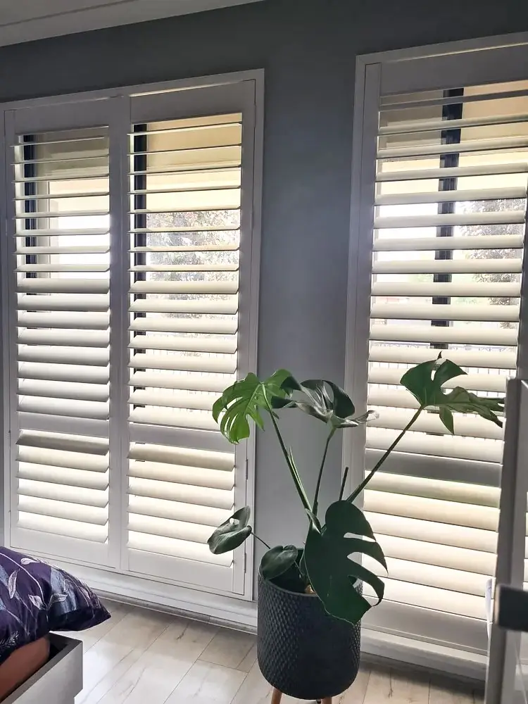 Two windows in a bedroom with plantation shutters on them