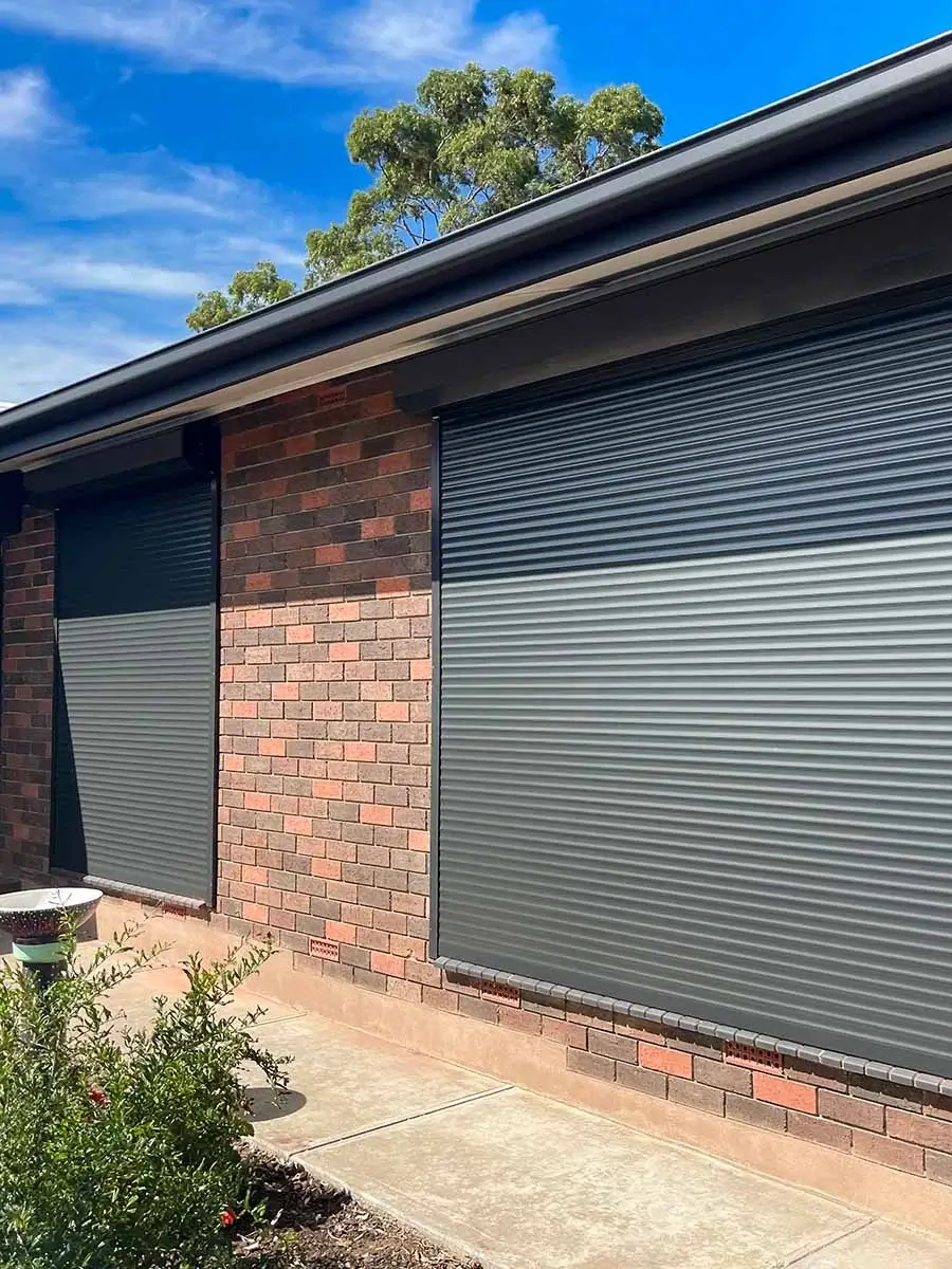 two grey roller shutters on a red brick home