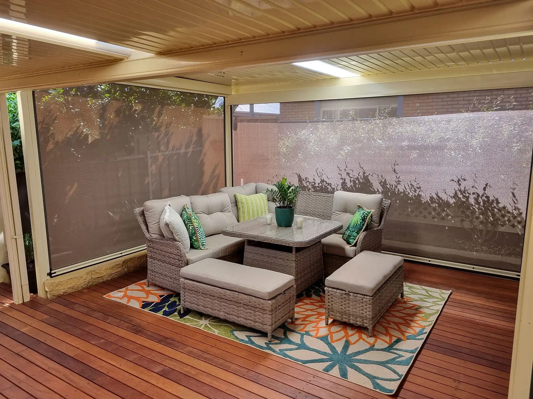 Outdoor seating area on a wooden deck, featuring comfortable wicker furniture and colourful cushions, enclosed by outdoor blinds for added shade and privacy.
