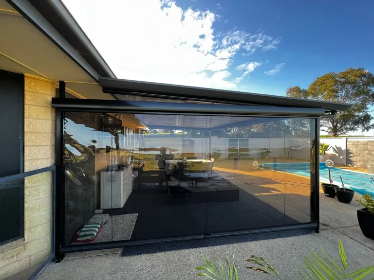 Modern outdoor patio area with transparent cafe blinds, overlooking a swimming pool and garden, featuring comfortable seating and a barbecue