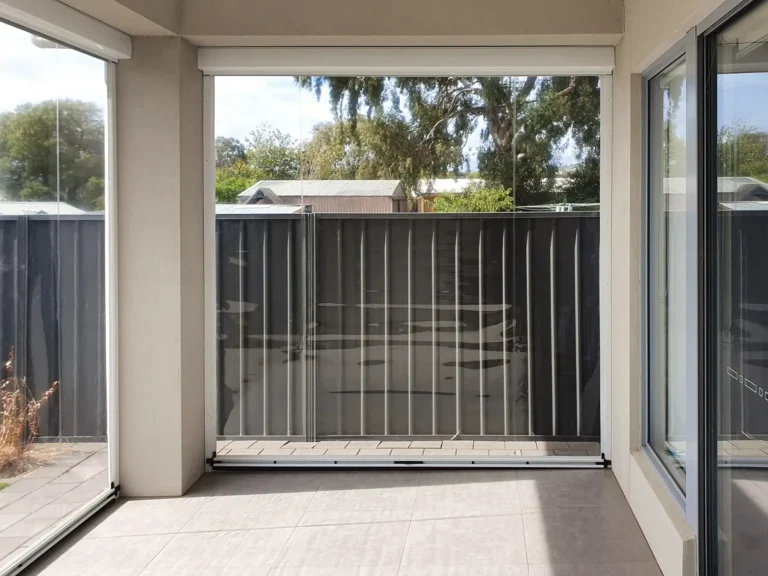 Enclosed patio area with transparent cafe blinds, providing a clear view of the garden and neighboring structures, with tiled flooring and metal fencing.
