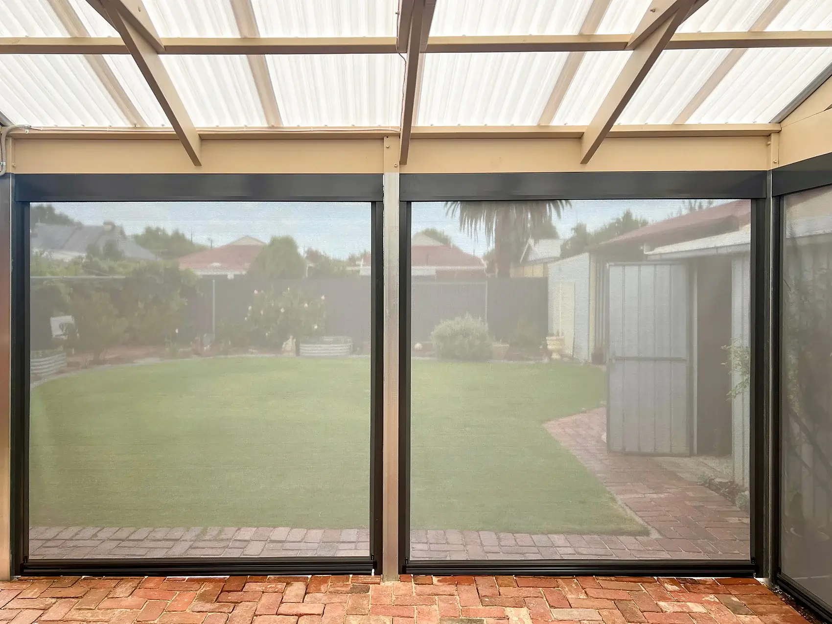 Enclosed patio area with outdoor blinds, providing shade and privacy while allowing a clear view of the backyard and garden area with a brick pathway.