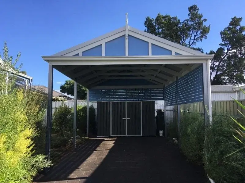 Backyard with a timber pergola carport featuring a gabled roof and lattice sides, providing shelter over a paved area leading to a garden shed.