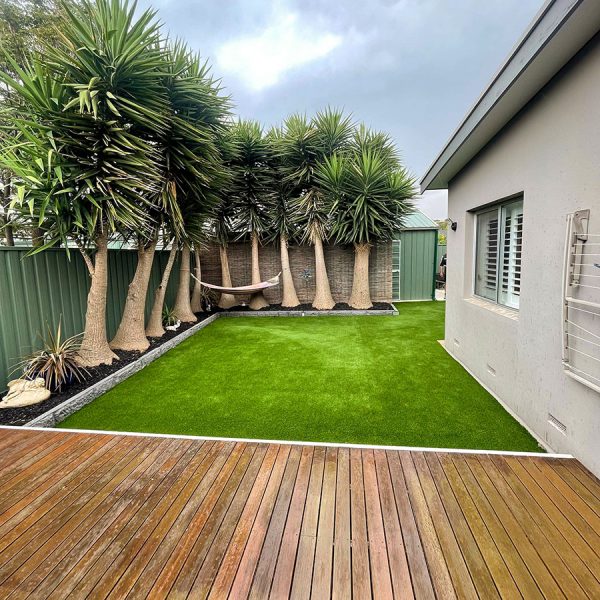artificial turf next to decking and a garden in a backyard